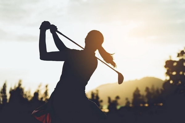 eine Silhouette einer Frau , die bei Sonnenuntergang mit einem Golfschläger spielt