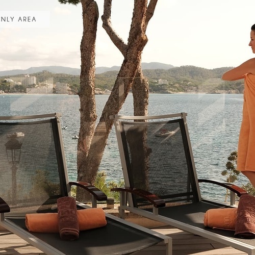 Eine Frau steht neben Liegestühlen und schaut auf das Meer