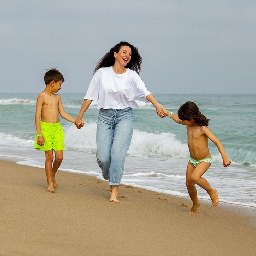 una mujer y dos niños caminan por la playa tomados de la mano