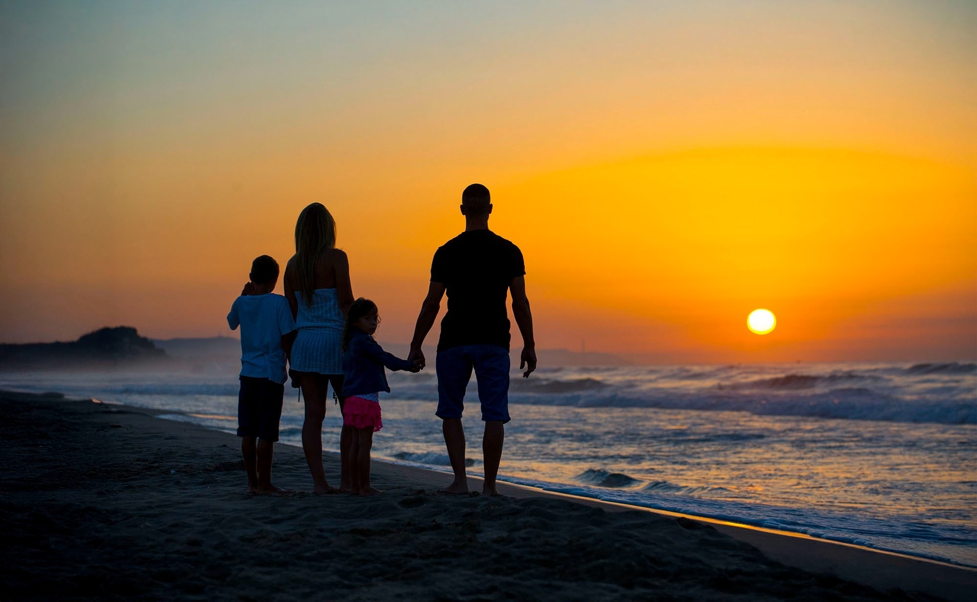 a family stands on the beach watching the sun set