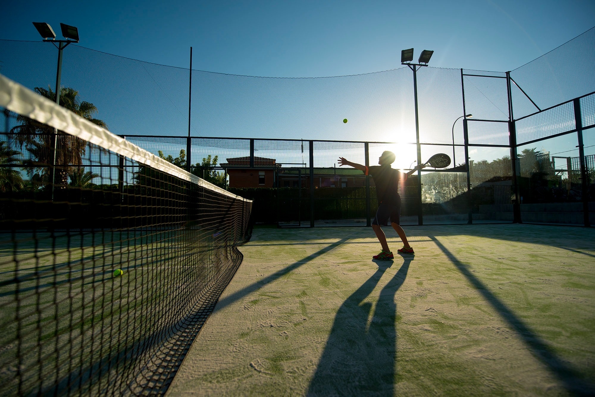un hombre está jugando al pádel en una cancha al atardecer