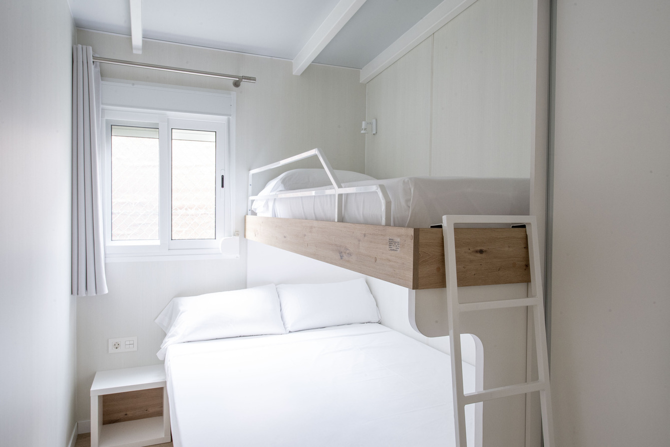 Chambre familiale avec lits superposés, vue sur fenêtre et rideau. Idéal pour Creixell camping & family resort.