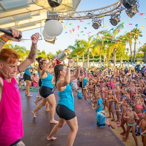 un grupo de niños bailan en un escenario mientras un hombre sostiene un micrófono