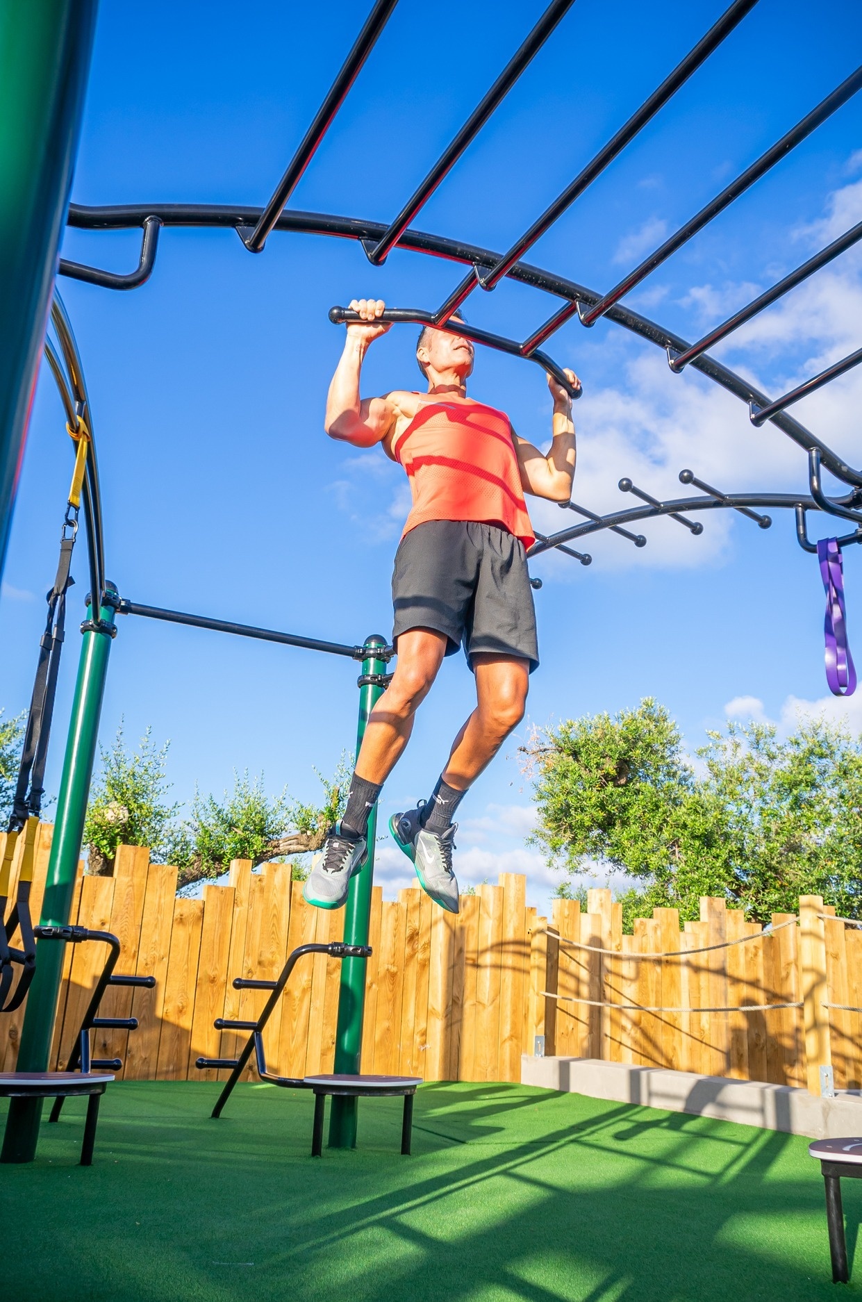un hombre en una camiseta roja y pantalones cortos negros está haciendo dominadas en una barra de ejercicios