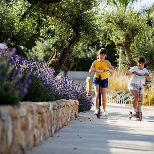 dos niñas montan scooters en un camino de hormigón