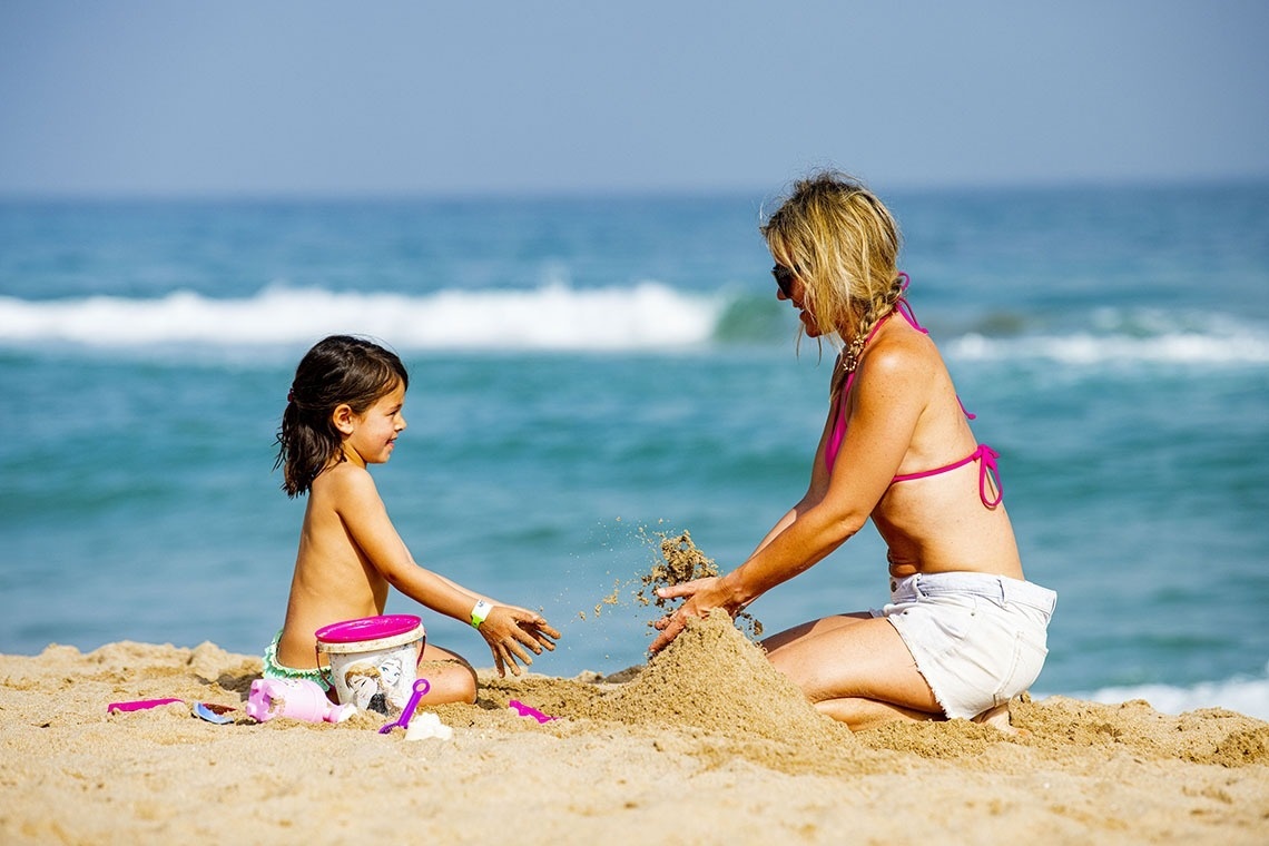 una mujer y una niña juegan con arena en la playa