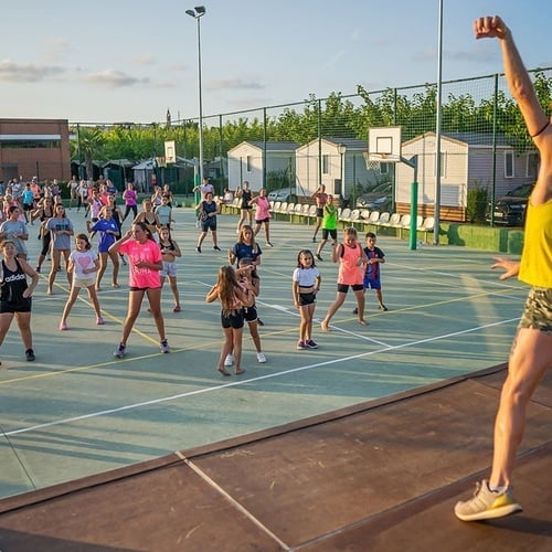 un hombre con una camiseta amarilla con un sol en la espalda está bailando con un grupo de niños en una cancha de baloncesto