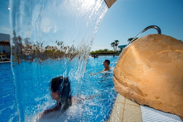un hombre y una mujer nadan bajo una cascada en una piscina