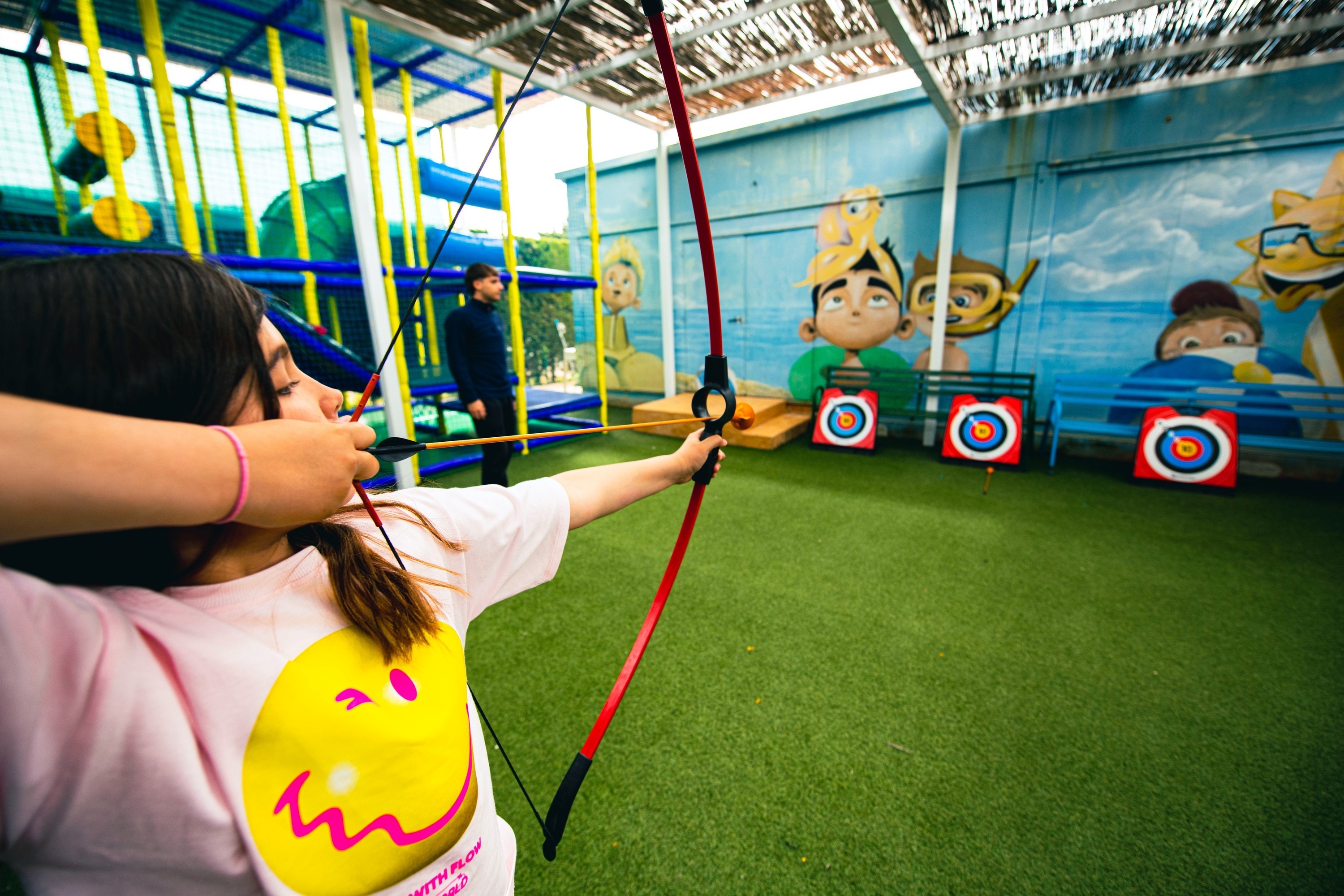 una niña sostiene un arco y una flecha frente a un mural de dibujos animados