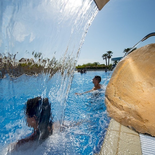 un hombre nadando bajo una cascada en una piscina