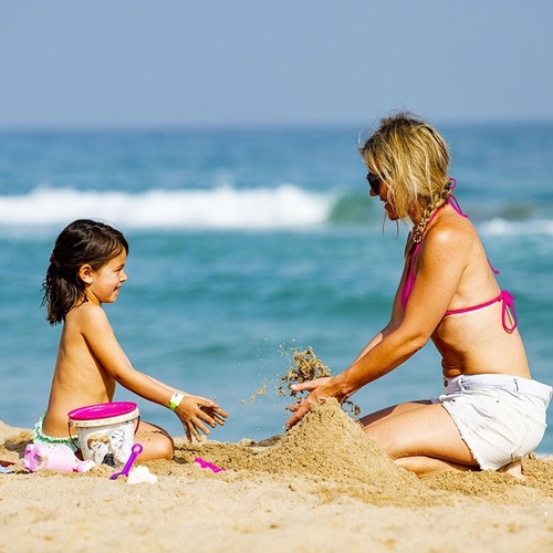una mujer y una niña juegan con arena en la playa