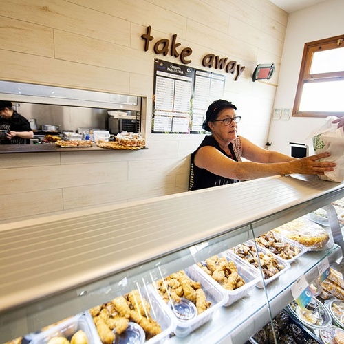 una mujer sostiene una bolsa de comida en una tienda de comestibles con la palabra take away en la pared