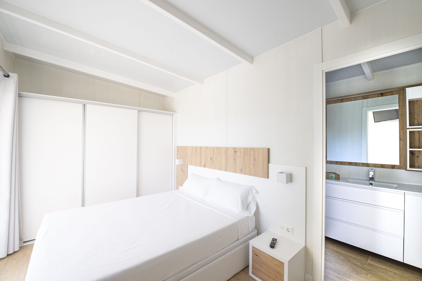 Chambre d'hôtel lumineuse avec lit blanc, placards et salle de bain. Idéal pour votre Creixell camping & family resort.