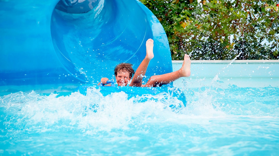 Un nen somriu mentre es llisca per un tobogan aquàtic a Creixell camping & family resort.