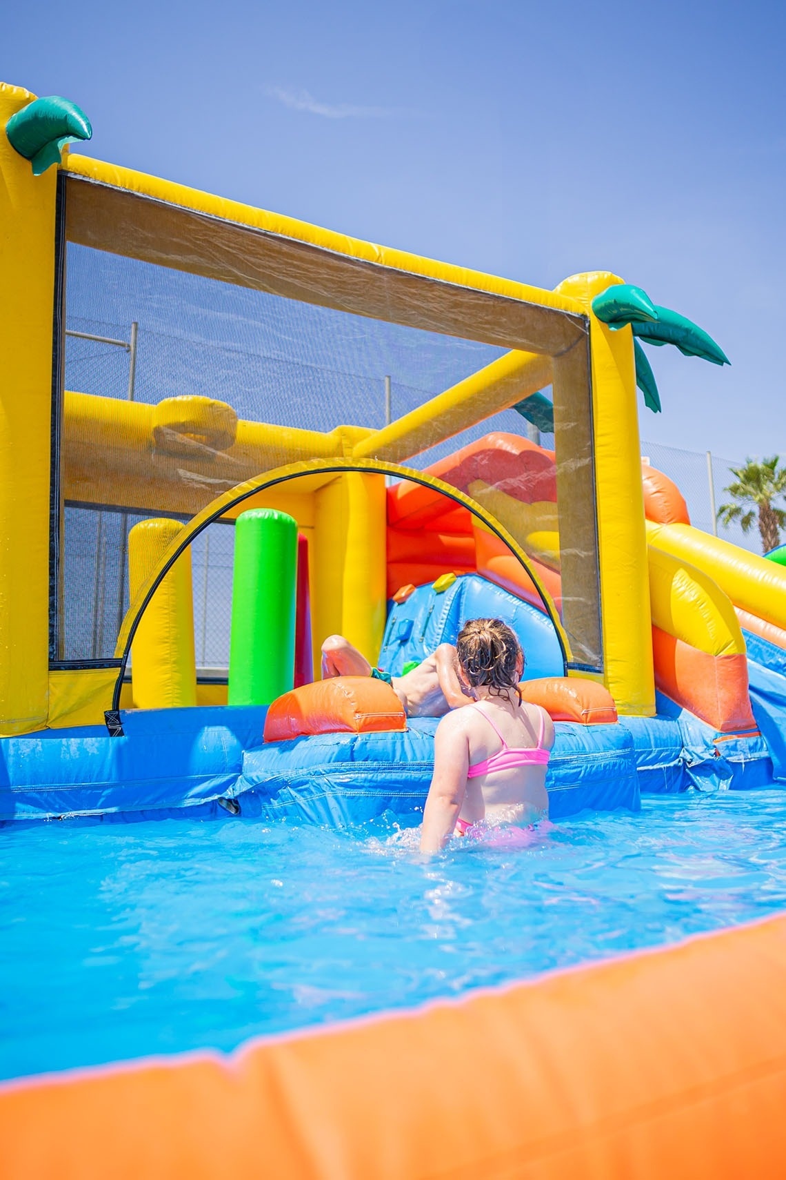una niña se sienta en la piscina frente a un castillo hinchable
