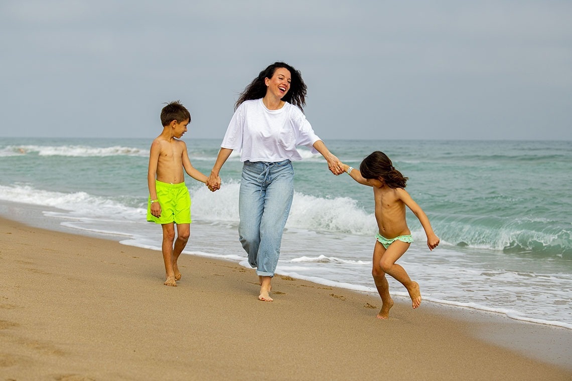 una mujer y dos niños caminan por la playa tomados de la mano