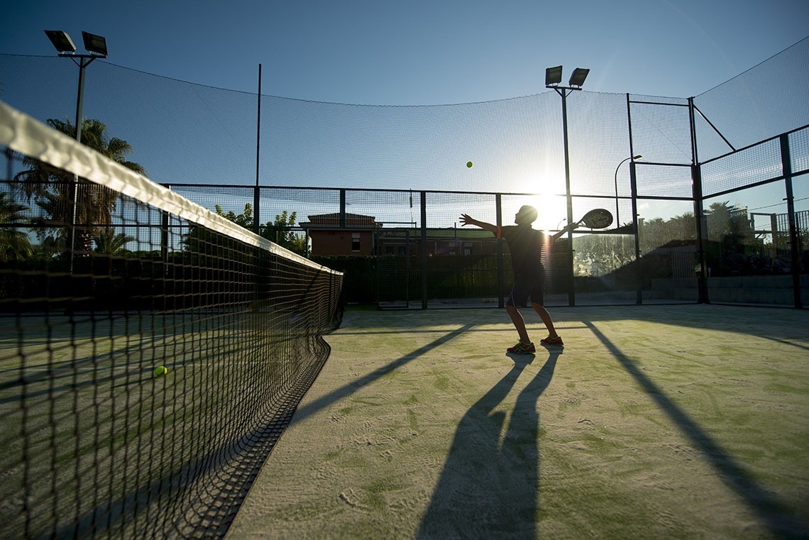 un hombre está jugando al pádel en una cancha al atardecer