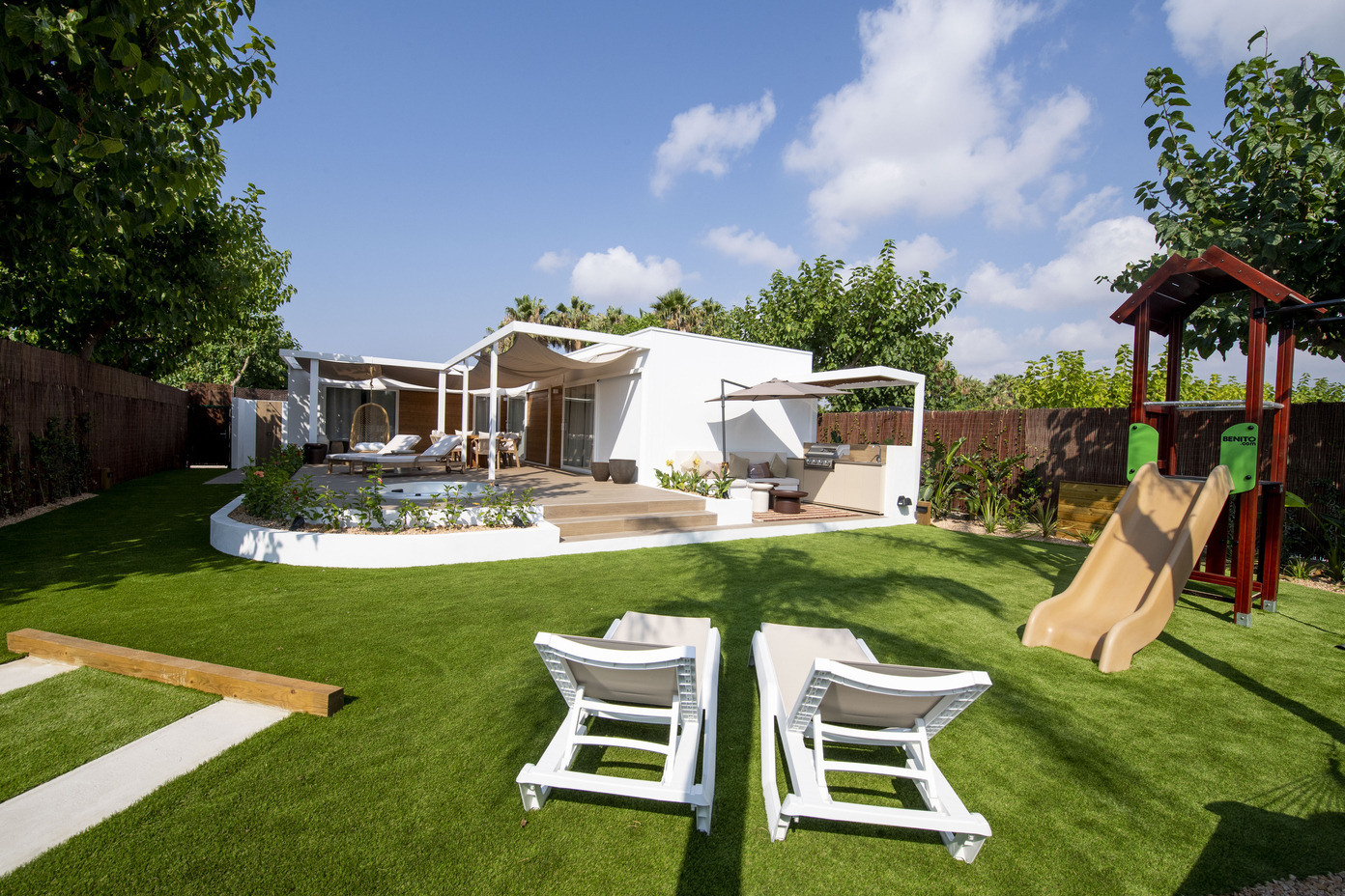 Jardin luxuriant avec toboggan et chaises longues, idéal pour des vacances 'Creixell camping & family resort'.