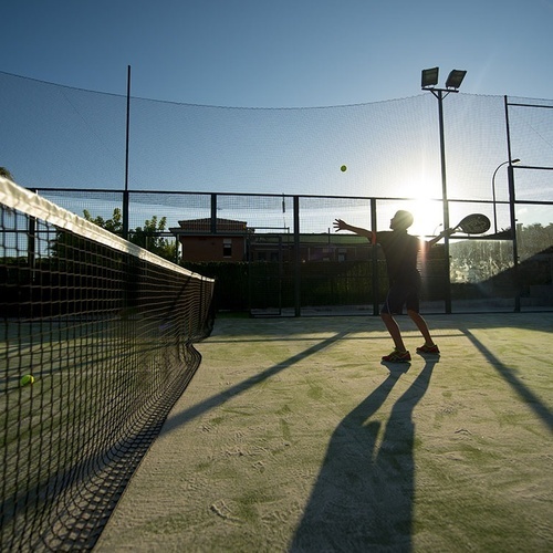 un hombre está jugando al pádel en una cancha al atardecer