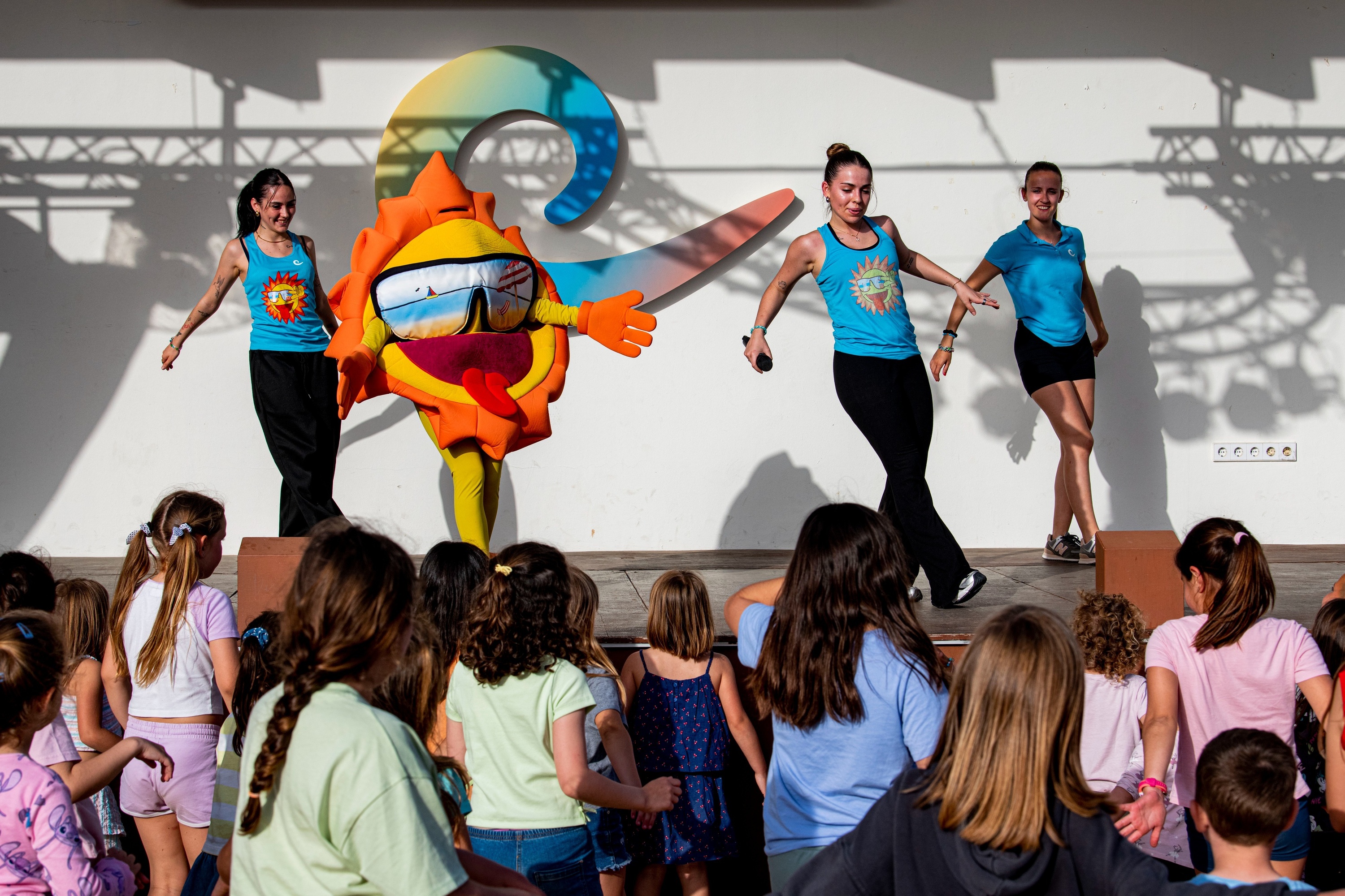 un grupo de niños bailan en un escenario con una mascota de sol