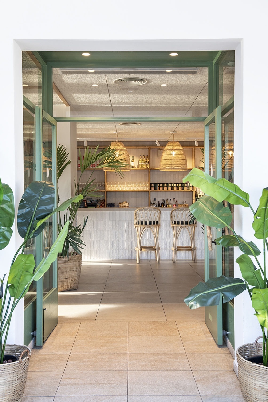 una puerta verde conduce a un restaurante con una barra y sillas de mimbre