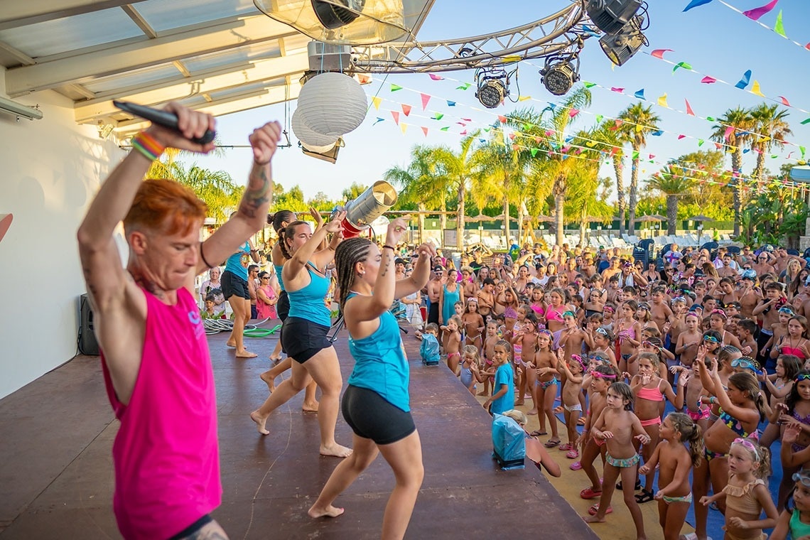 un grupo de niños bailan en un escenario mientras un hombre sostiene un micrófono