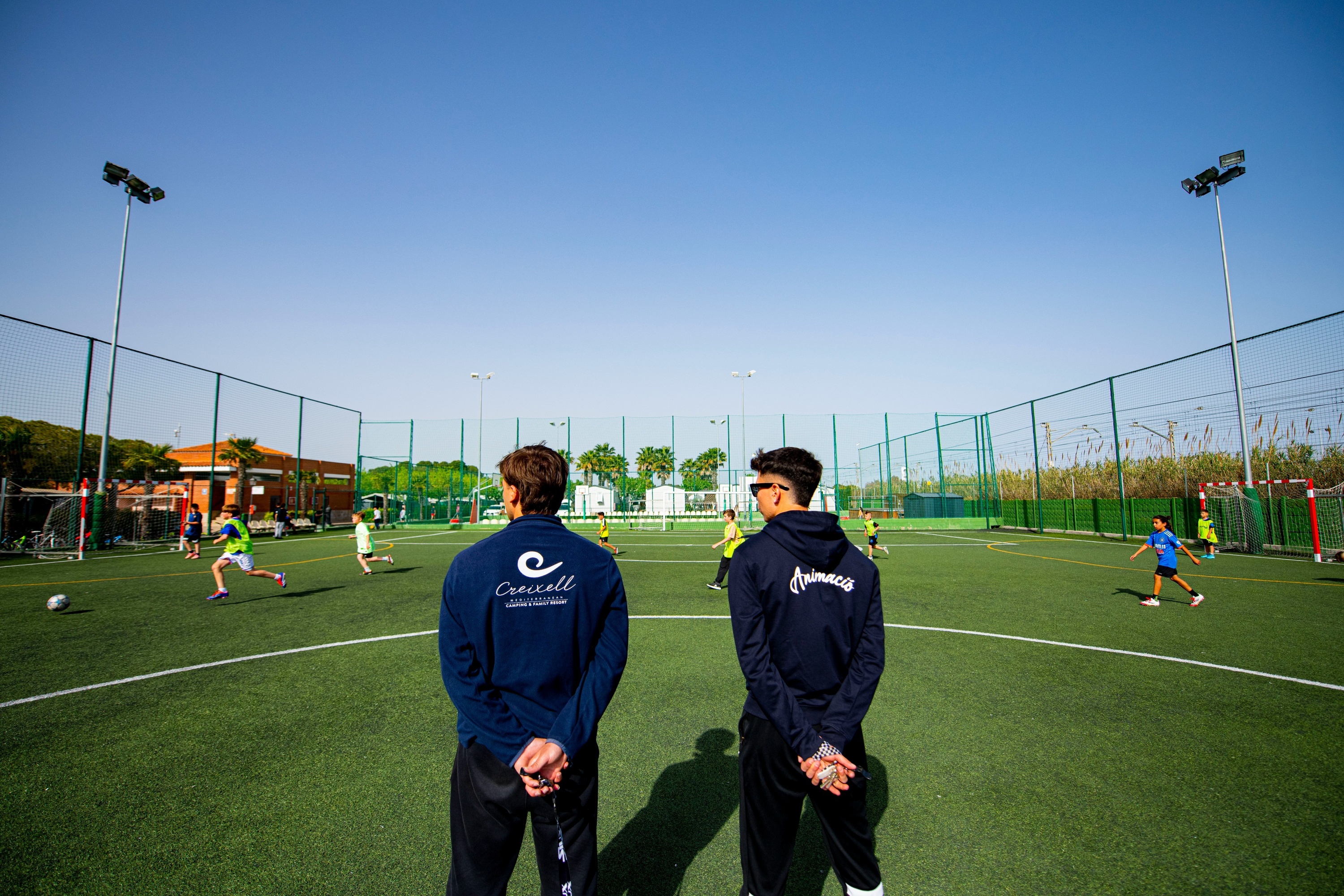 dos hombres miran a los niños jugando al fútbol en un campo de fútbol