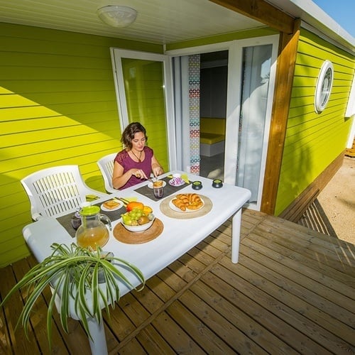 una mujer se sienta en una mesa con comida frente a una casa verde