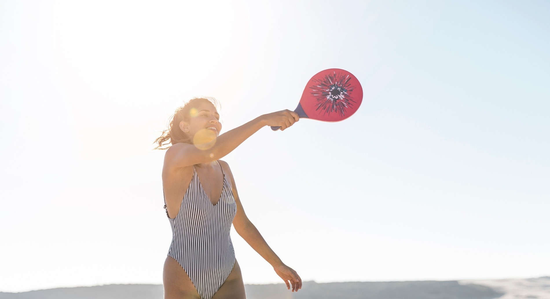 una mujer con un traje de baño a rayas sostiene una paleta roja con la palabra raqueta en la parte superior