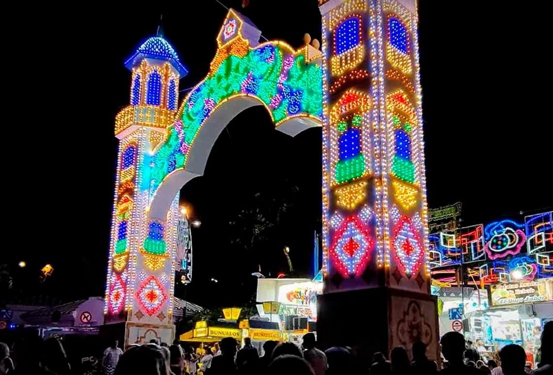 una multitud de personas se reúnen alrededor de un arco decorado con luces de colores