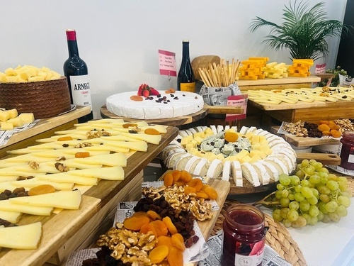 Un suntuoso bufé presenta una amplia variedad de quesos, acompañados de frutos secos, nueces, uvas, mermelada y botellas de vino.