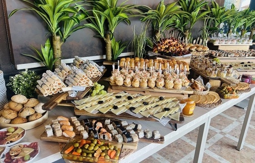 Una mesa de buffet está profusamente decorada con una gran variedad de aperitivos, incluyendo sushi, tablas de quesos, panes y otros bocadillos, creando un festín visual.