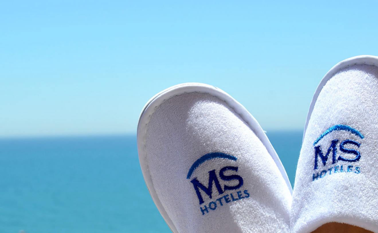 un par de pantuflas blancas con el logotipo de ms hoteles