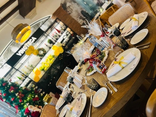 Una mesa festiva adornada con regalos y decoraciones navideñas está preparada en una vinoteca o restaurante.