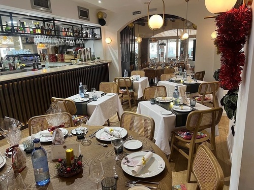 El interior de un restaurante elegantemente decorado y preparado para una celebración, con mesas servidas y una barra de bebidas.