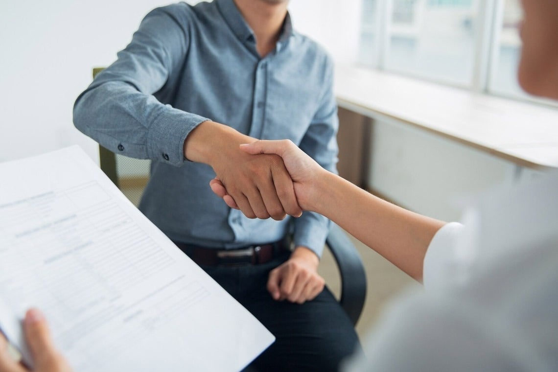 a man in a blue shirt shakes hands with a woman holding a piece of paper