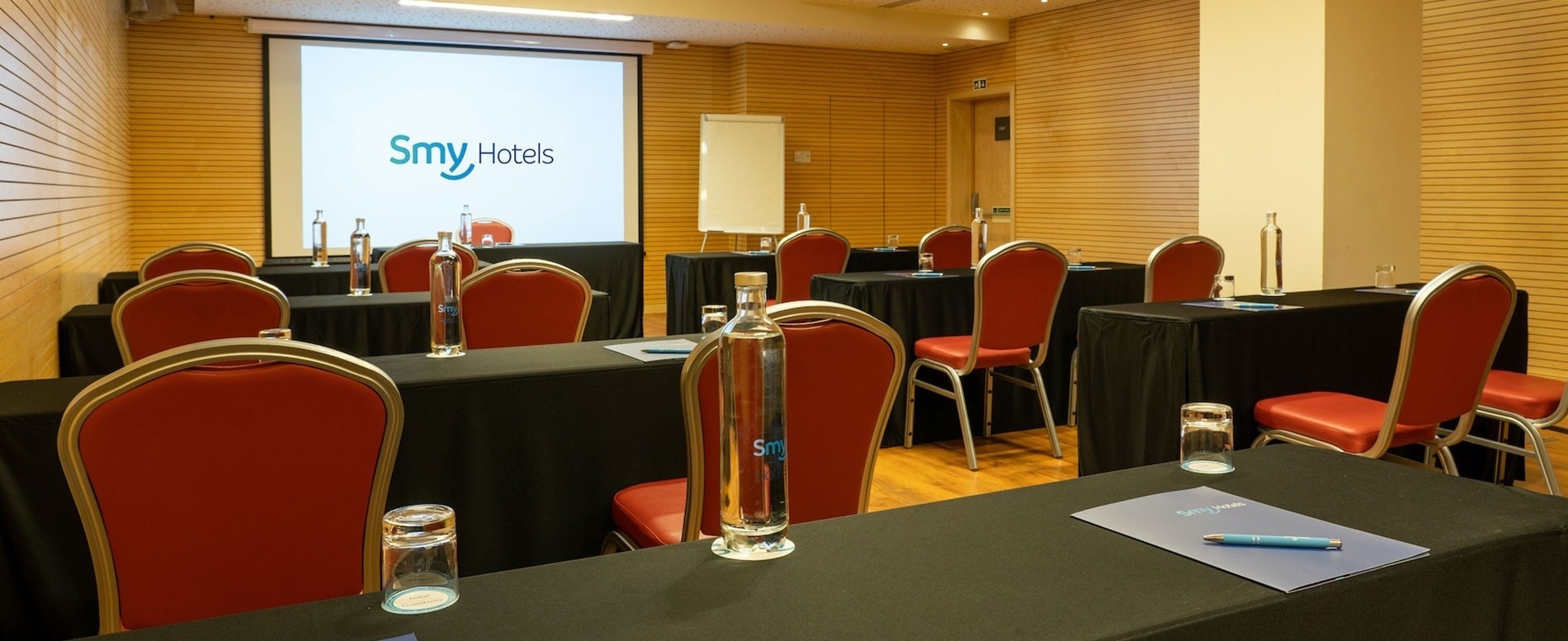 a room with tables and chairs and a screen that says smy hotels