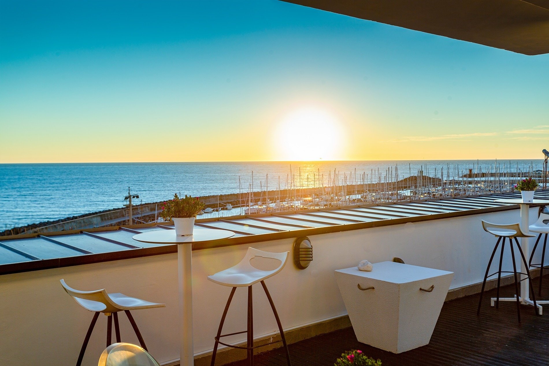 uma varanda com mesas e banquetas com vista para o oceano ao pôr do sol