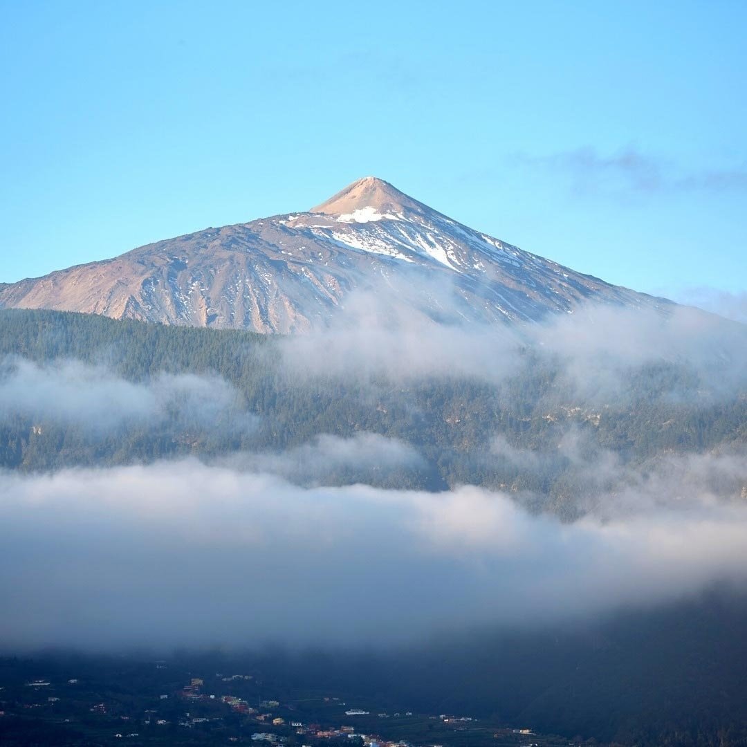 una montagna coperta di neve è circondata da nuvole e alberi