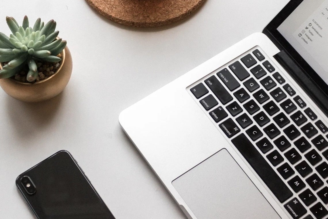 un computer portatile è seduto su un tavolo accanto a un telefono e una pianta