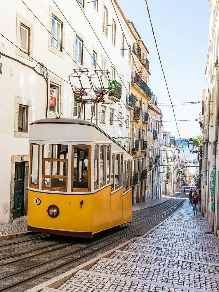 un treno giallo e bianco viaggia lungo una strada acciottolata