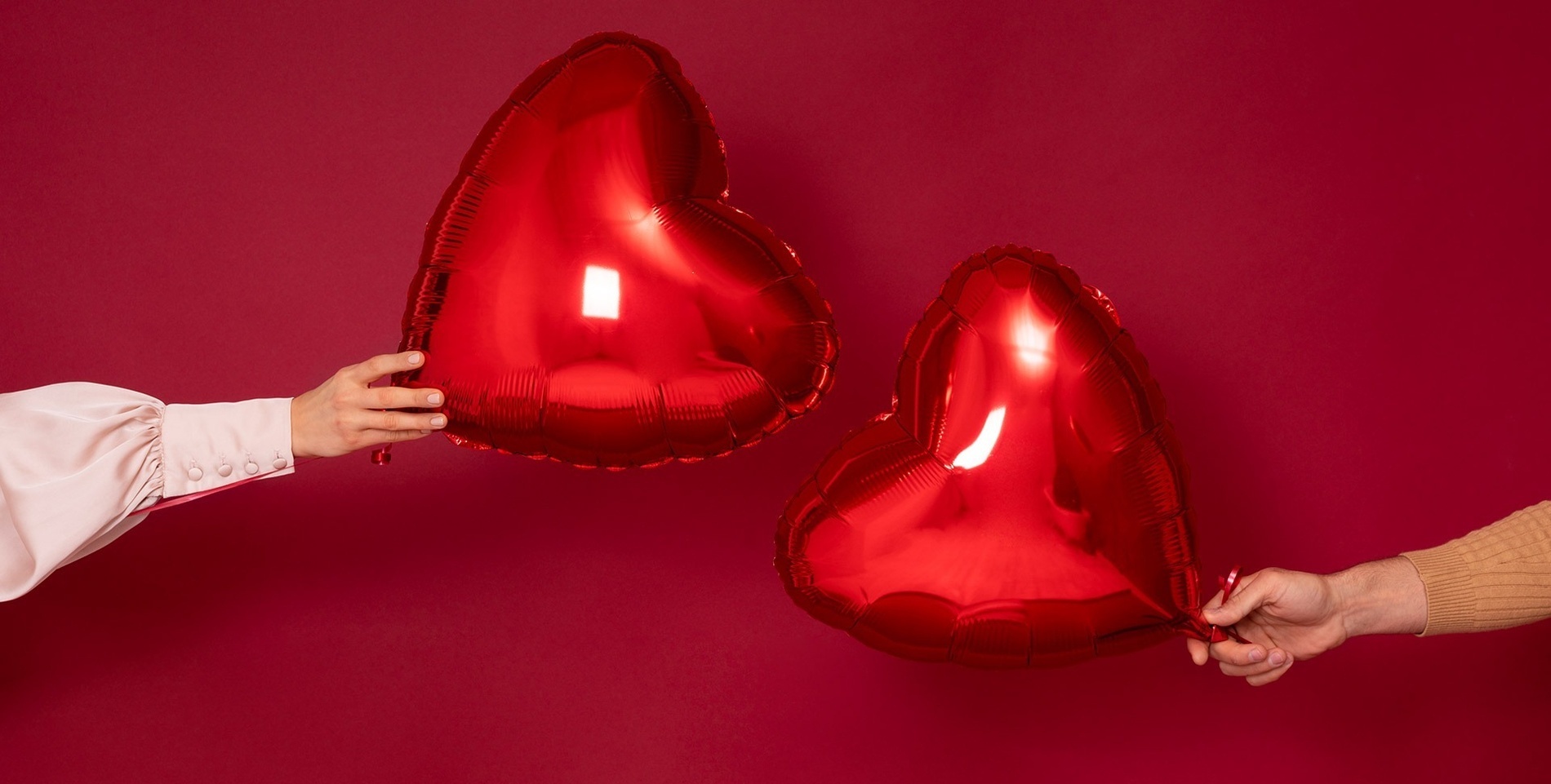 two people holding red heart shaped balloons on a red background