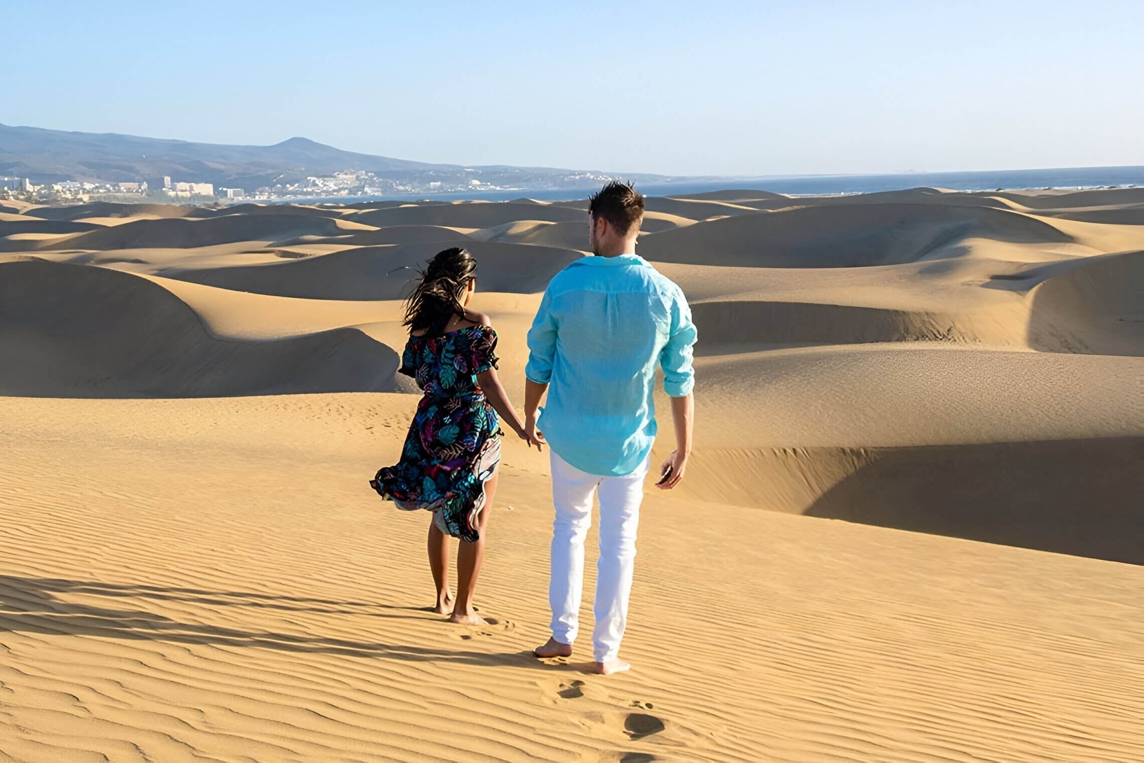 un hombre y una mujer sostienen las manos mientras caminan por el desierto