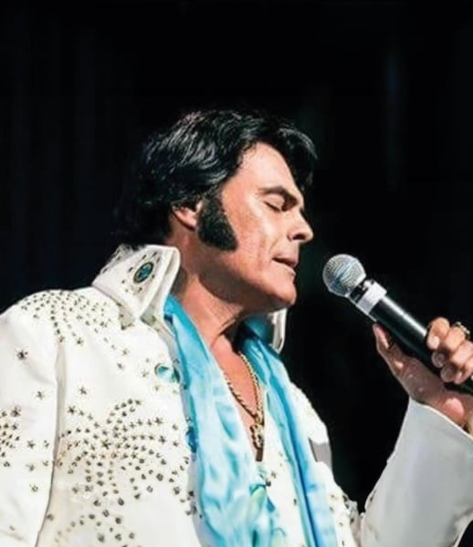 a man in a white suit is singing into a microphone .