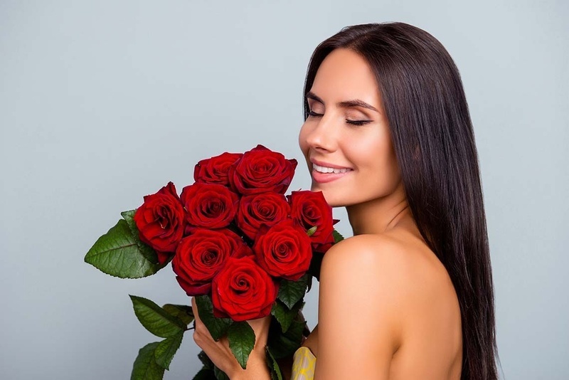 a woman smelling a bouquet of red roses with her eyes closed