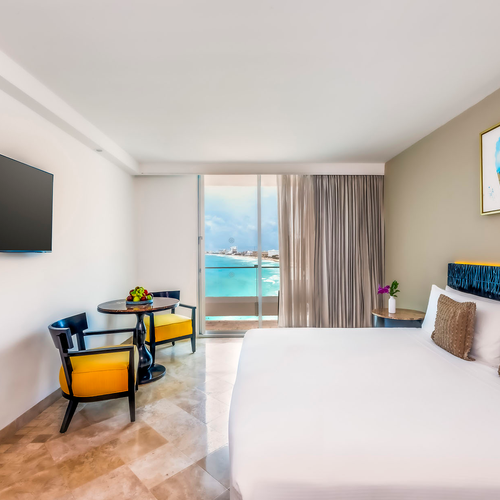 Modern hotel room with ocean view, king bed, sitting area, and flat-screen TV. DEMO 3