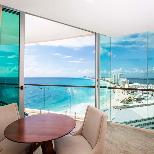 Balcony view of beach and ocean from a hotel room with dining table and chairs. DEMO 3