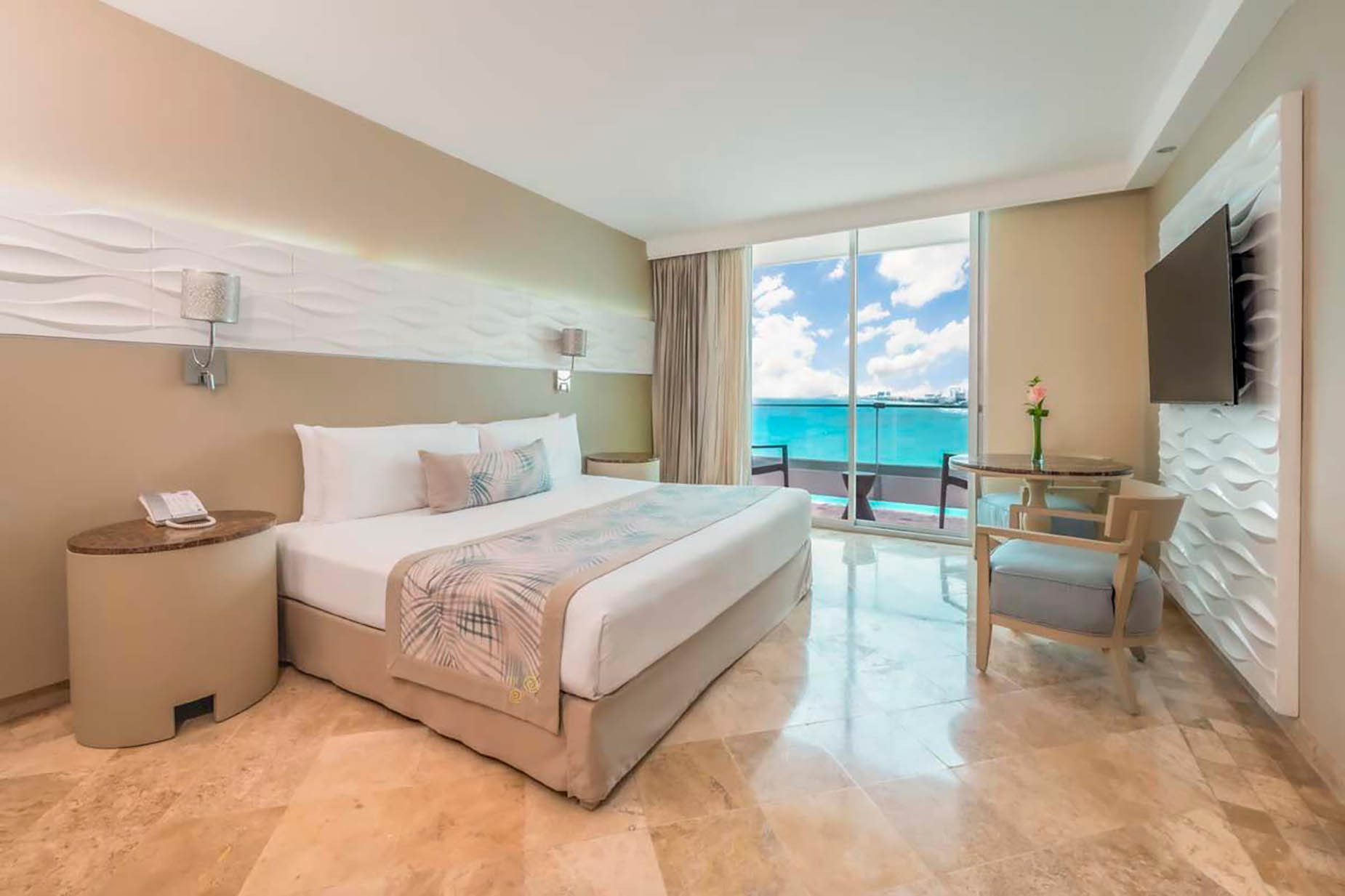 Luxury hotel room with king bed, ocean view balcony, and seating area. DEMO 3