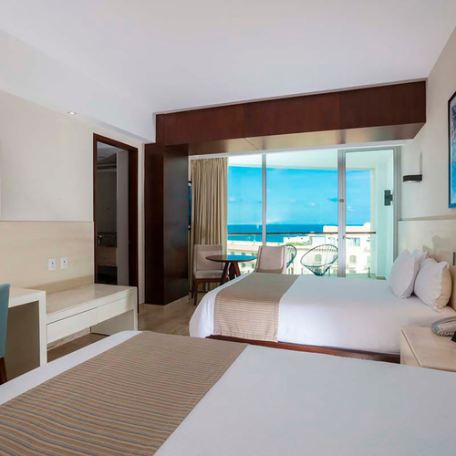 Hotel room with two beds, desk, and ocean view balcony. DEMO 3