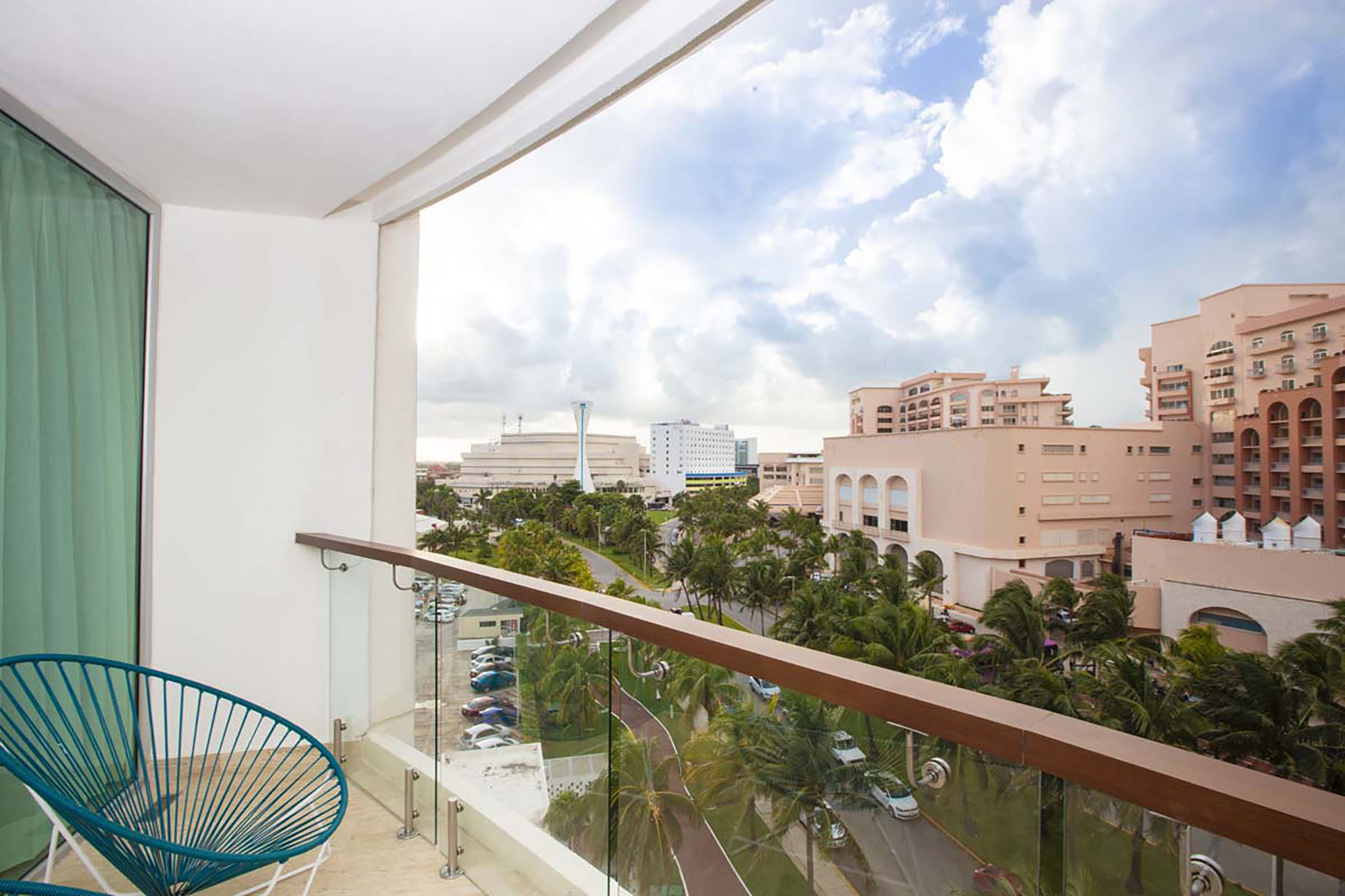 Hotel balcony view with palm trees, resort buildings, and a sky with clouds. DEMO 3